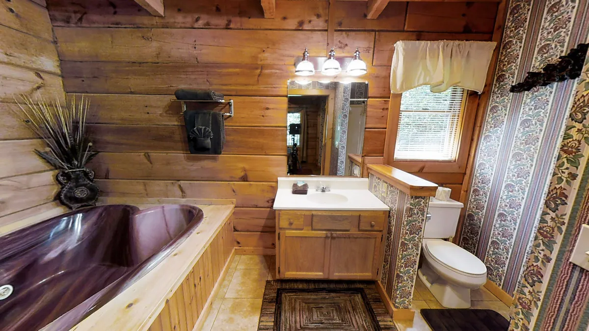 This interior image features a spacious, heart-shaped bathtub set within a wood-accented alcove. The surrounding vanity, mirror, and plush towels add an inviting, spa-like ambiance. Decorative wallpaper and soft lighting enhance the mood, making the space ideal for a romantic soak after exploring the outdoors.