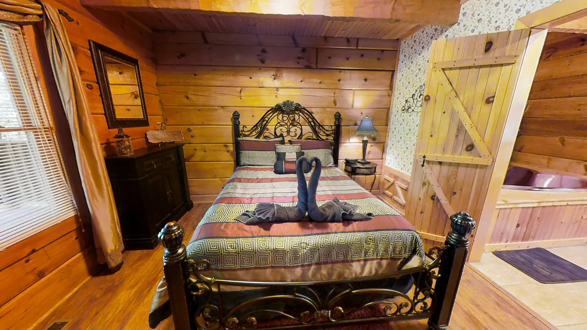 A cozy primary bedroom featuring a queen-sized bed adorned with decorative pillows, soft linens, and a wooden accent wall. Natural light filters in, creating a warm and restful atmosphere ideal for relaxation or romance. A mirror and door add dimension and a sense of privacy.