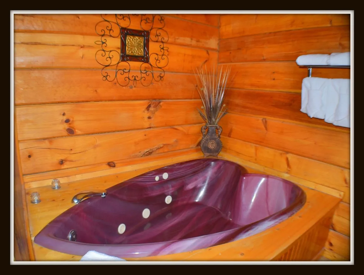 A heart-shaped jacuzzi tub set against rustic wooden walls, with plush towels and tasteful decorative wall art. The space evokes a sense of luxury and intimacy, inviting guests to unwind in a candle-lit bubble bath.