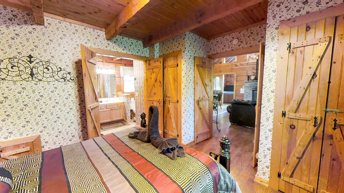 A warm, inviting bedroom with a cozy striped bedspread, wooden doors, and ornate metal wall decor. The scene suggests a welcoming spot for relaxing evenings, whether reading or simply unwinding by the fire, with hints of natural light that evoke the peaceful setting.