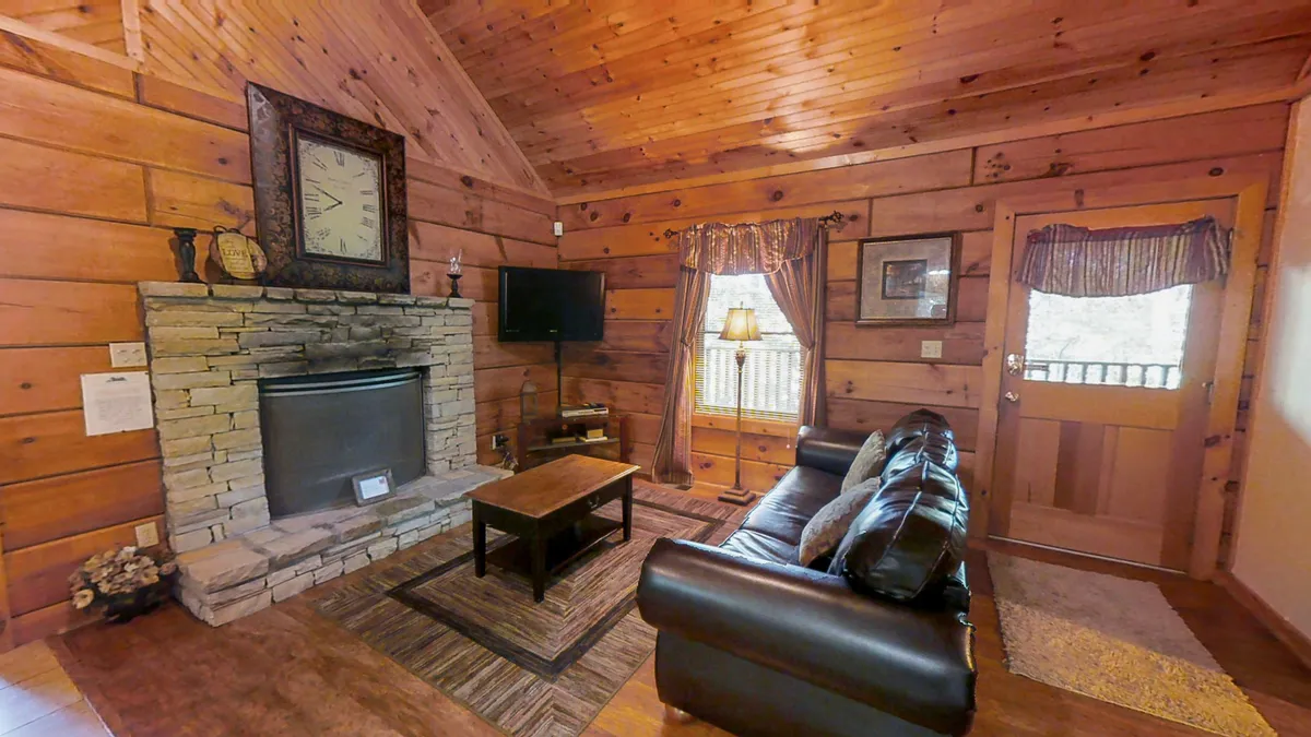 The image shows a cozy living space centered around a stone fireplace, with a comfortable leather sofa facing a flat-screen TV. Warm wooden accents and a soft, inviting atmosphere make it a perfect spot for relaxing, watching movies, or spending time with loved ones.